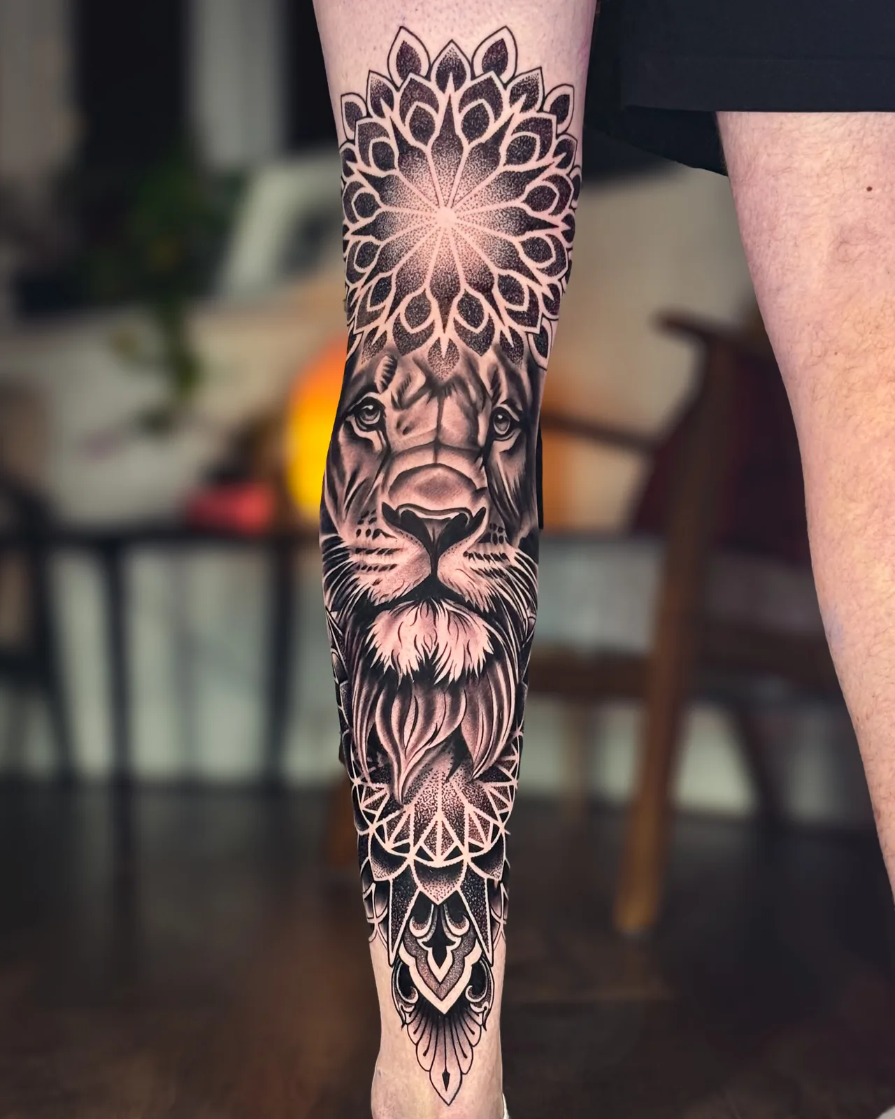Realistic lion framed by dotwork mandalas down the shin, leg tattoo by Scotty Massa